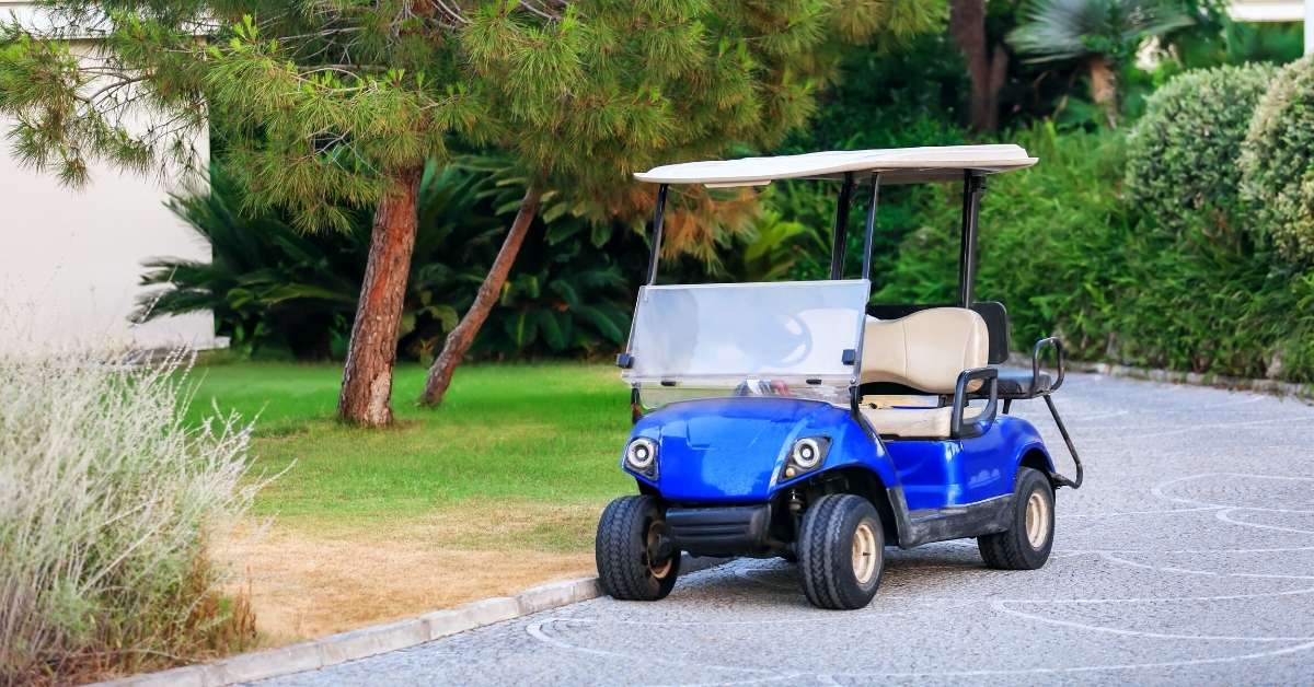 Blue golf cart parked on the side of the road within a resort with greenery in the background